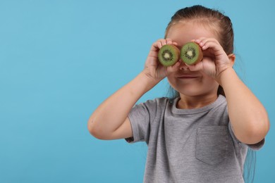 Photo of Girl covering eyes with halves of fresh kiwi on light blue background, space for text