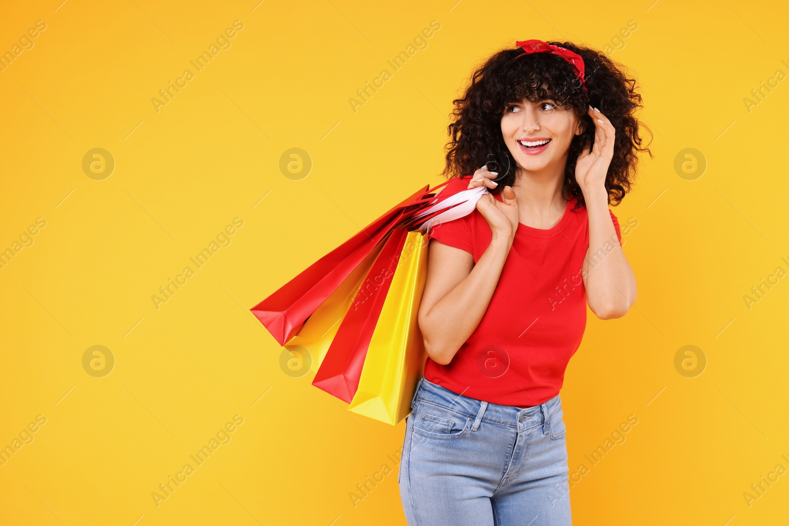 Photo of Happy young woman with shopping bags on yellow background