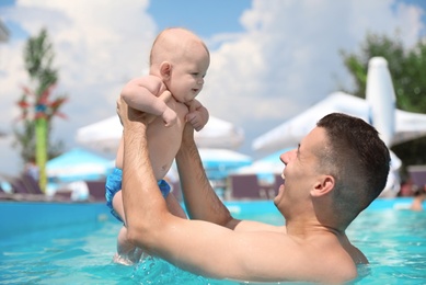 Man with his little baby in swimming pool on sunny day, outdoors