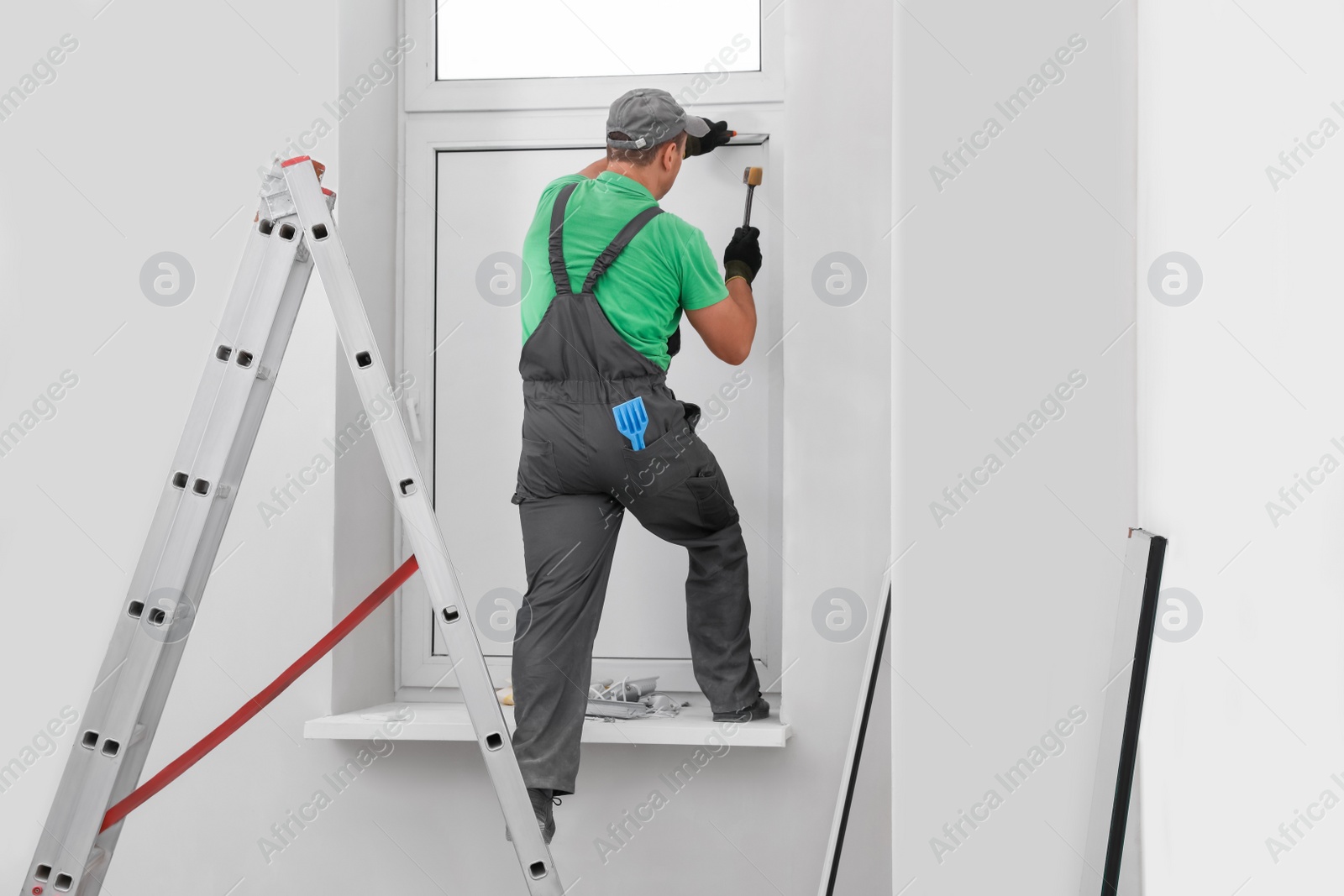 Photo of Worker in uniform installing double glazing window indoors, back view