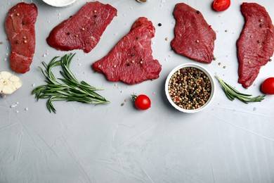 Fresh raw meat steaks and spices on light grey table, flat lay. Space for text