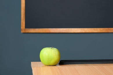 Photo of Wooden school desk and apple near blackboard on grey wall