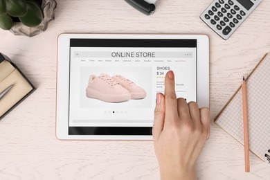 Photo of Woman with tablet shopping online at white wooden table, top view