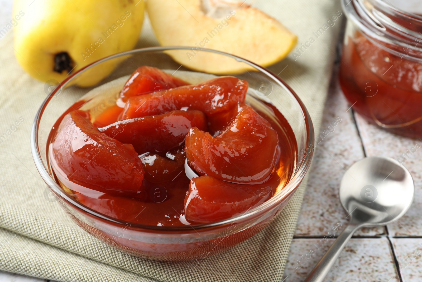 Photo of Tasty homemade quince jam in bowl and fruits on tiled table, closeup