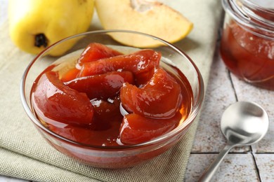 Photo of Tasty homemade quince jam in bowl and fruits on tiled table, closeup