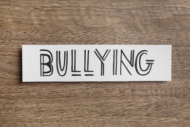 Photo of Paper card with word Bullying on wooden table, top view