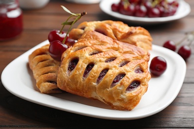 Photo of Fresh delicious puff pastry with sweet cherries served on wooden table