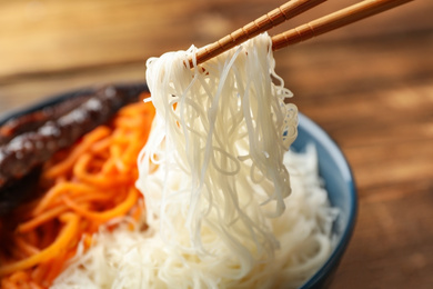 Photo of Chopsticks with tasty cooked rice noodles over bowl, closeup