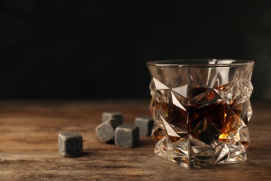 Photo of Golden whiskey in glass with cooling stones on table. Space for text