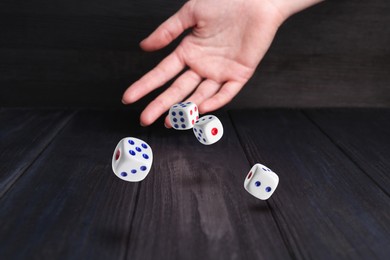 Image of Woman throwing white dice on black wooden table, closeup