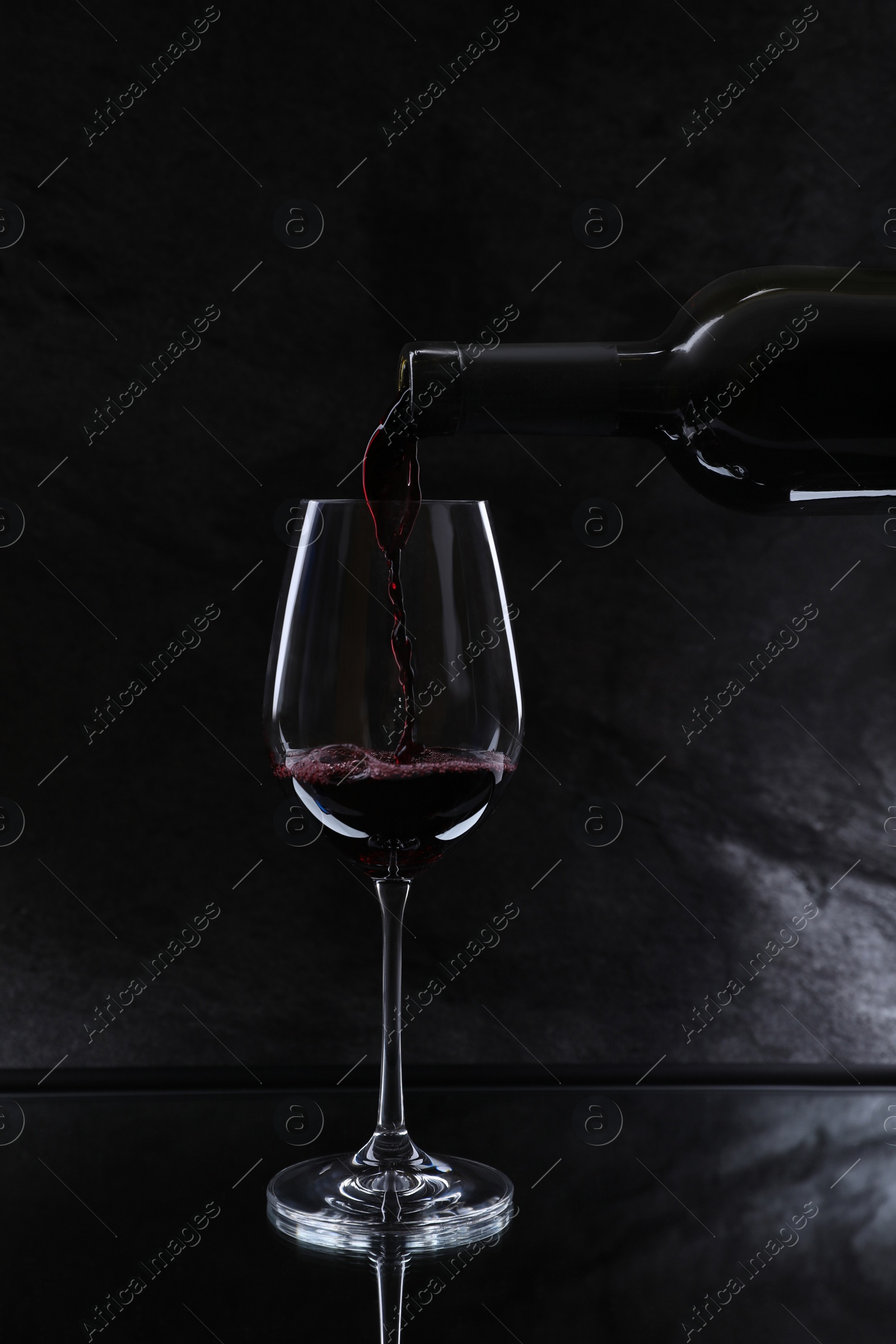 Photo of Pouring red wine from bottle into glass on black background