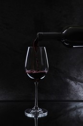 Pouring red wine from bottle into glass on black background