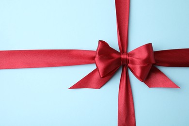 Photo of Red satin ribbon with bow on light blue background, top view