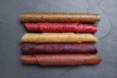 Photo of Delicious fruit leather rolls on black table, flat lay