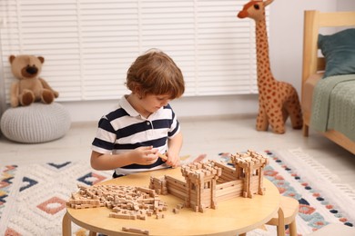 Photo of Little boy playing with wooden entry gate at table in room. Child's toy