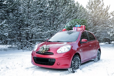 Photo of Car with Christmas tree, wreath and gifts in snowy forest on winter day