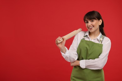 Photo of Happy professional confectioner in apron holding rolling pin on red background. Space for text