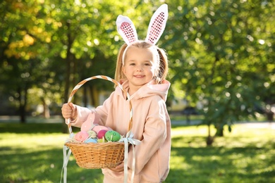 Cute little girl with bunny ears and basket of Easter eggs in park