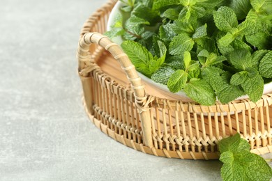Photo of Wicker tray with bowl of fresh green mint leaves on grey table, closeup. Space for text