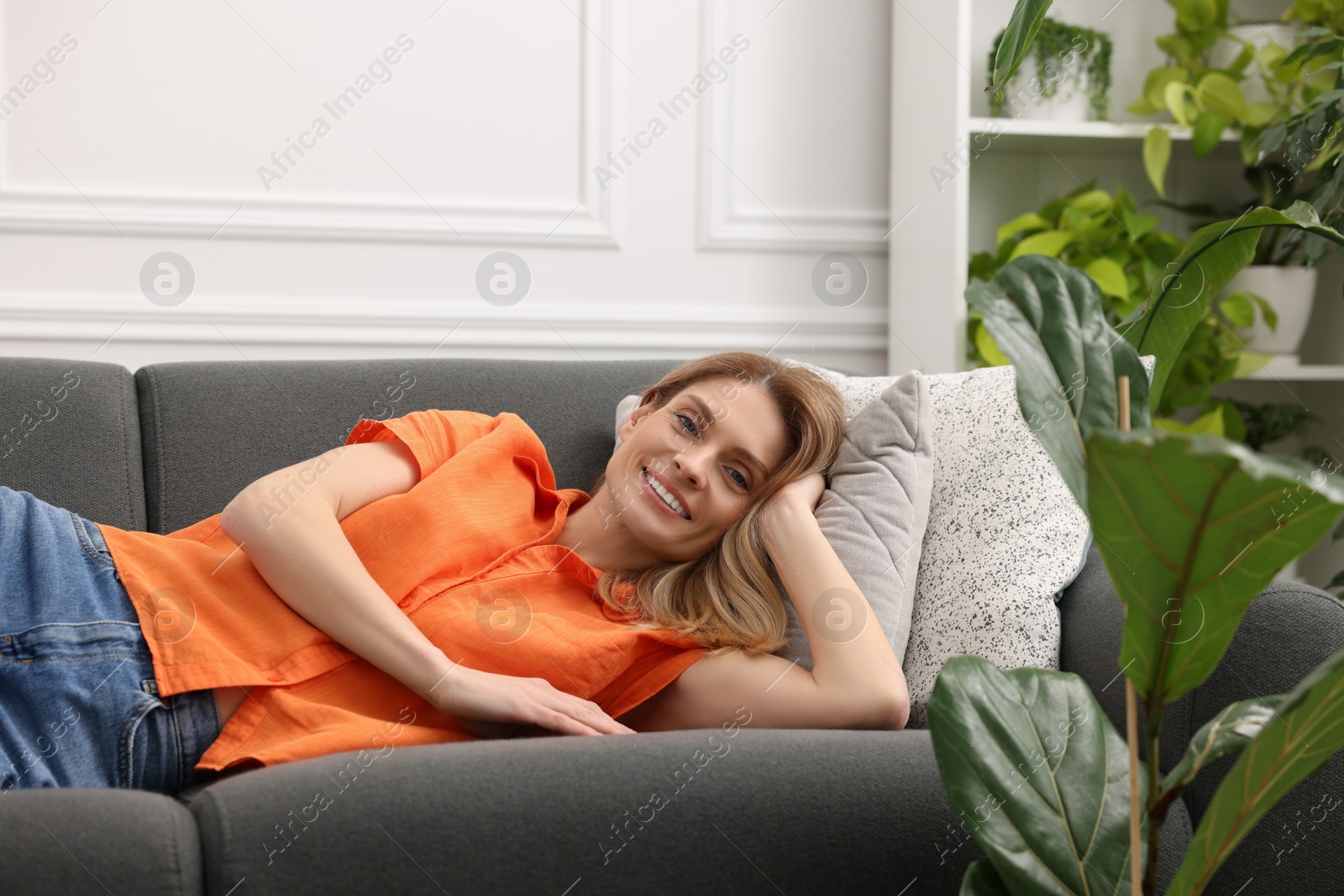 Photo of Woman relaxing on sofa in room with green houseplants