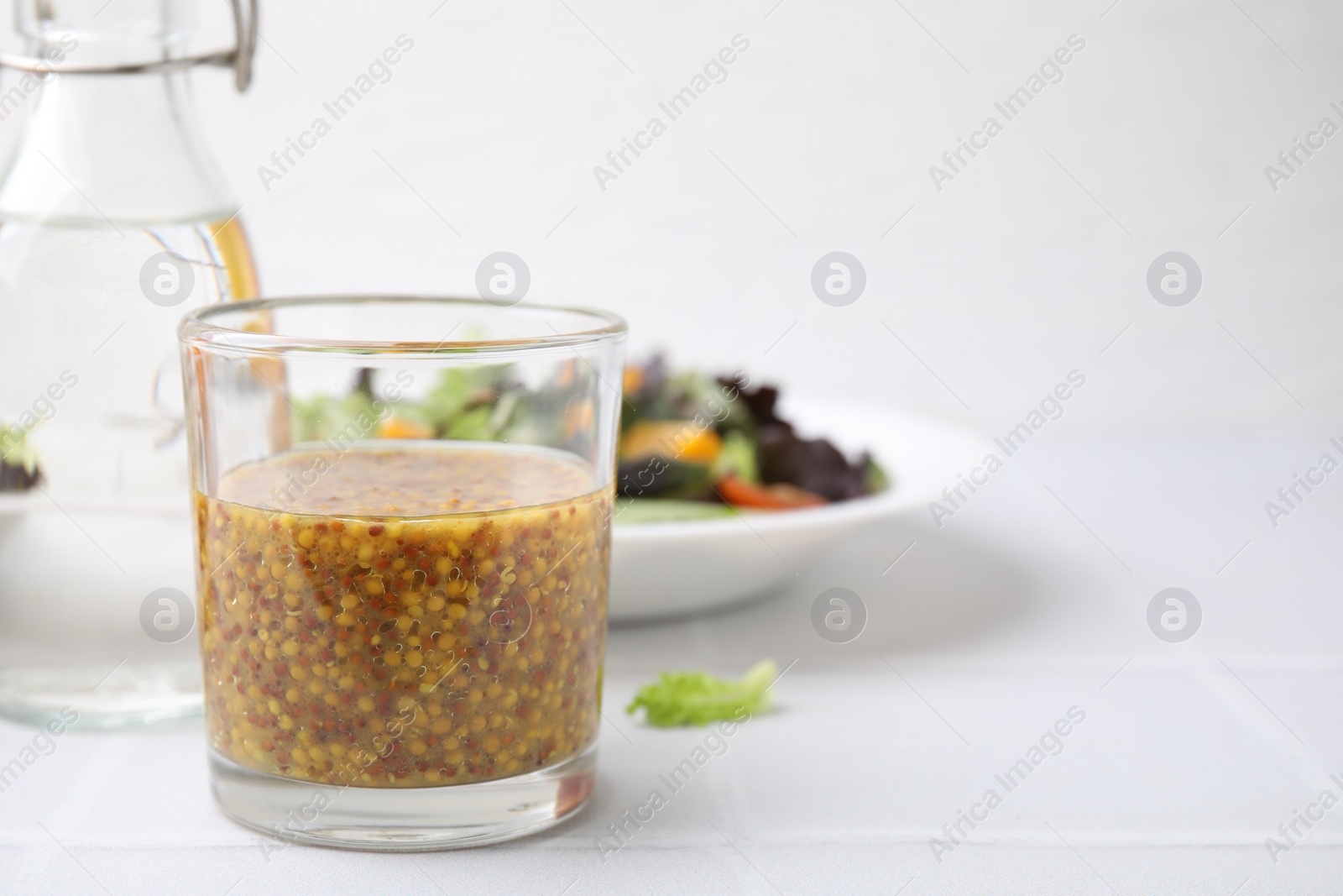 Photo of Tasty vinegar based sauce (Vinaigrette) in glass on light tiled table, closeup. Space for text