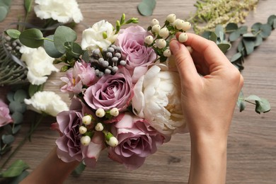 Florist creating beautiful bouquet at wooden table, closeup
