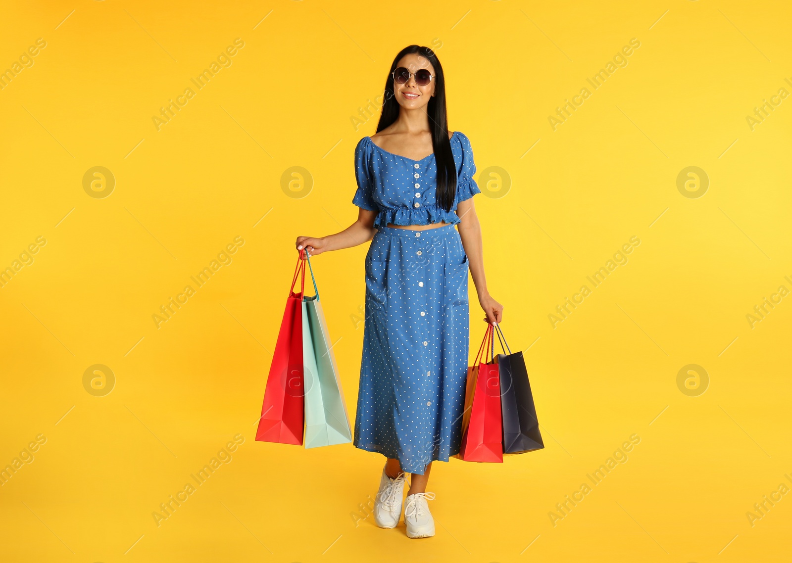 Photo of Beautiful young woman with paper shopping bags on yellow background