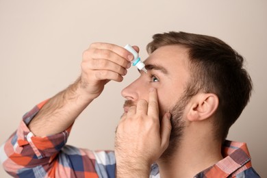 Photo of Young man using eye drops on beige background