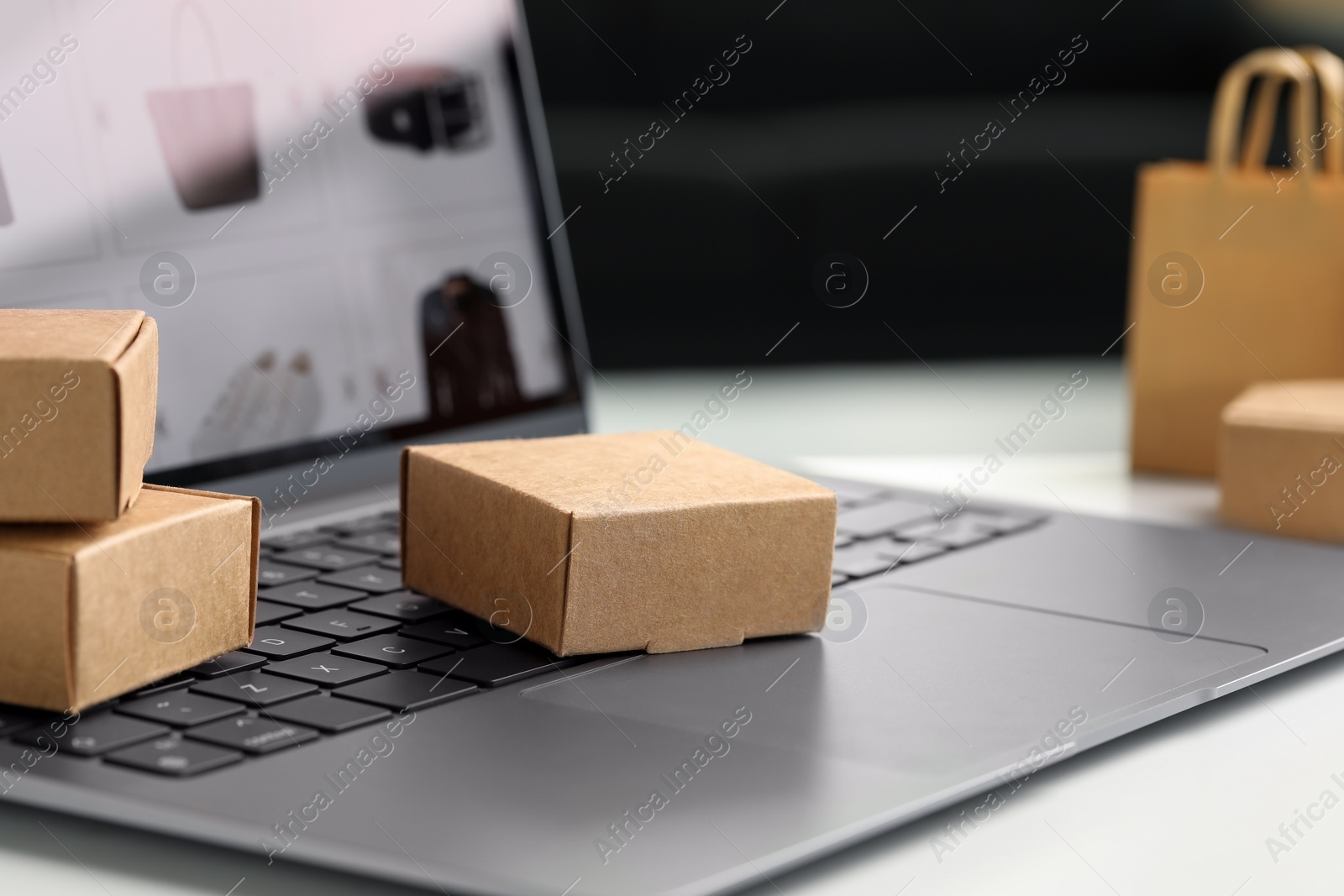 Photo of Online store. Small parcels and laptop on white table, closeup