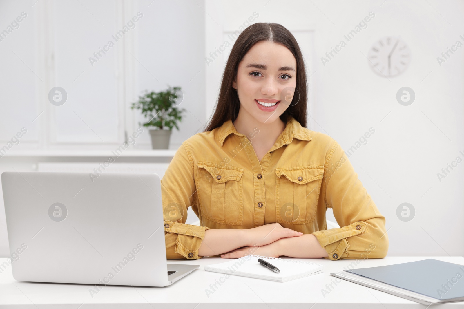 Photo of Young female intern working with laptop at table in office