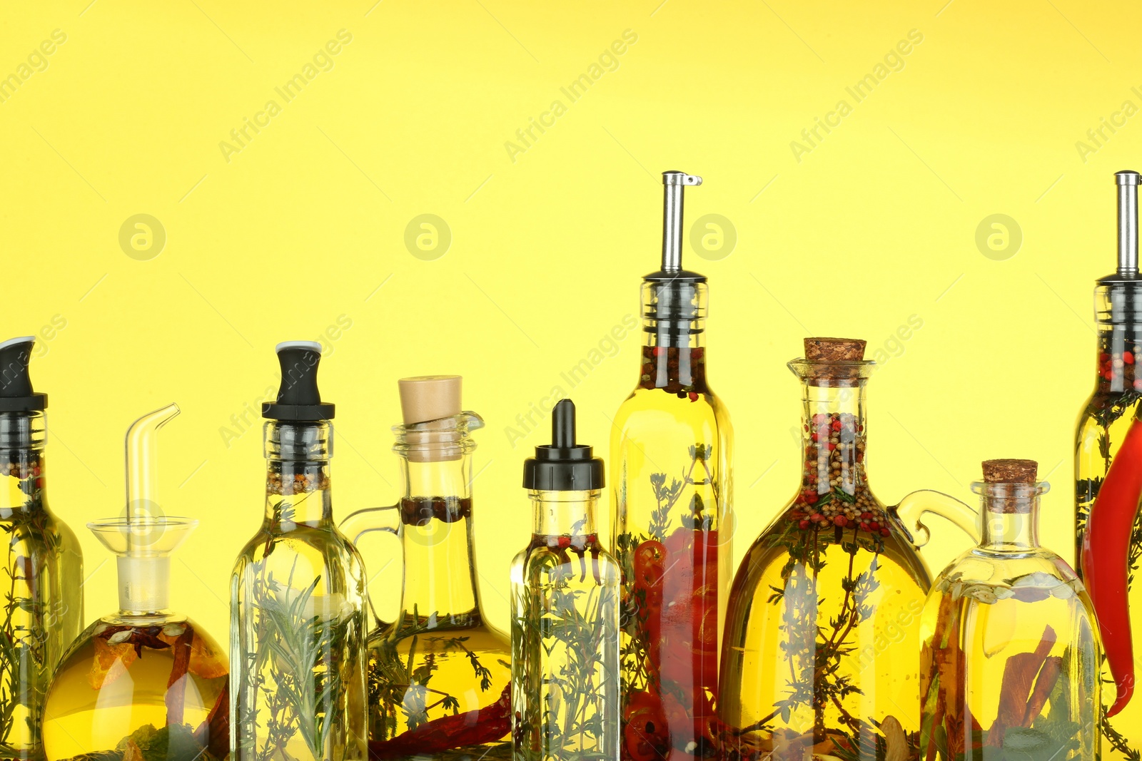 Photo of Cooking oil with different spices and herbs in bottles on yellow background