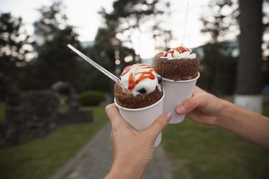 Photo of Couple holding delicious desserts with whipped cream on city street, closeup