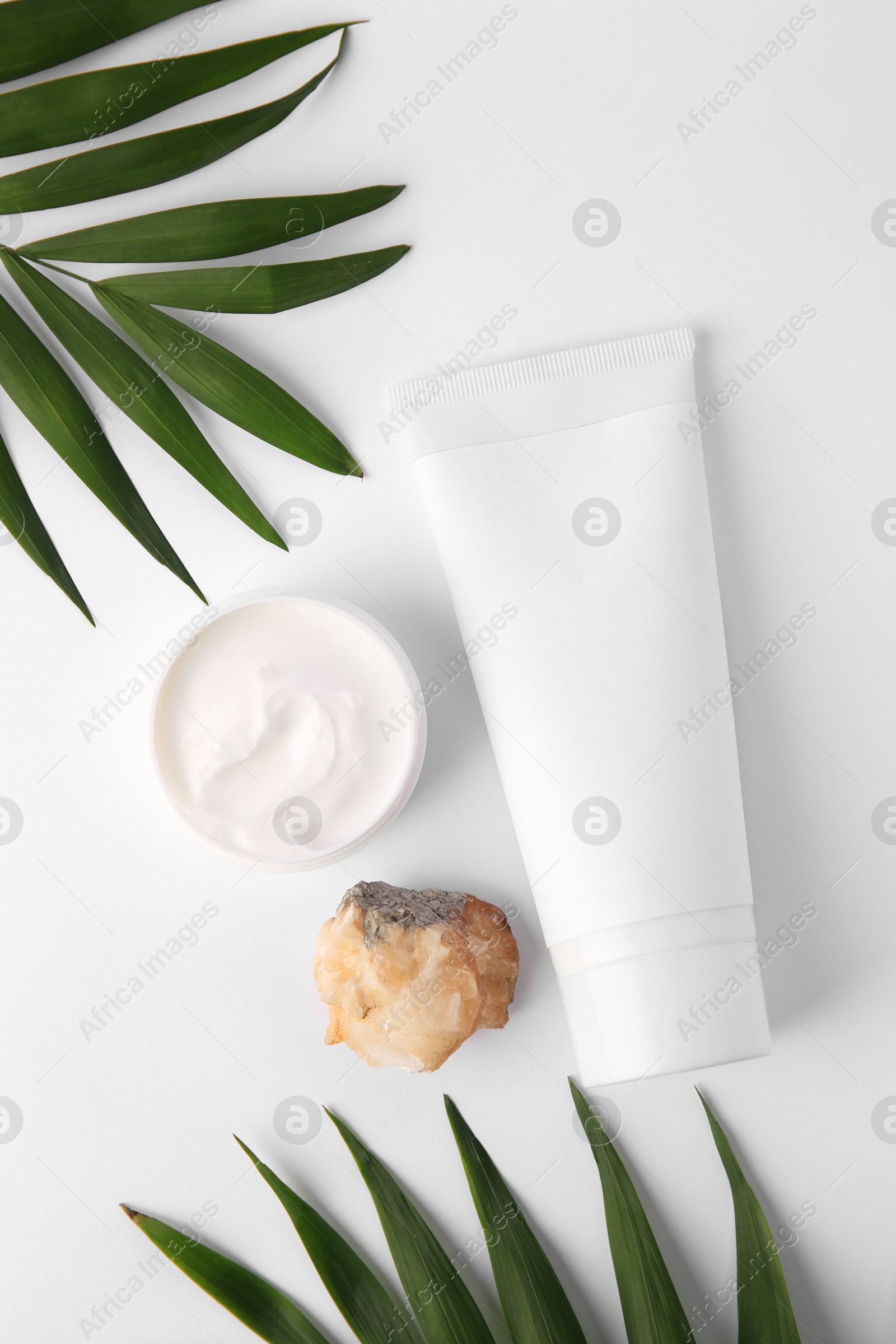 Photo of Cosmetic products, quartz gemstone and palm leaves on white background, flat lay