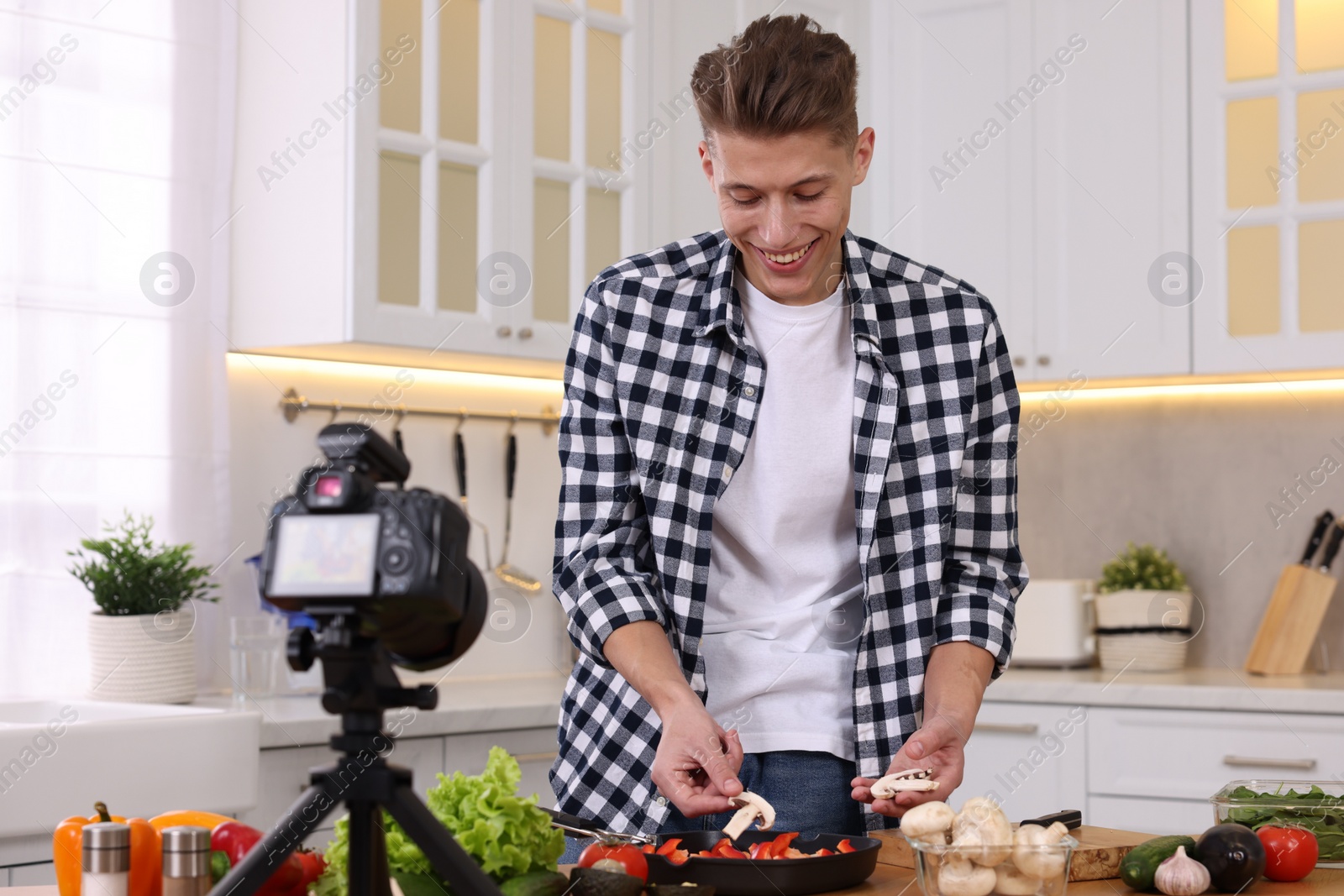 Photo of Smiling food blogger cooking while recording video in kitchen