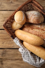 Photo of Wicker basket with different types of bread on wooden table, top view