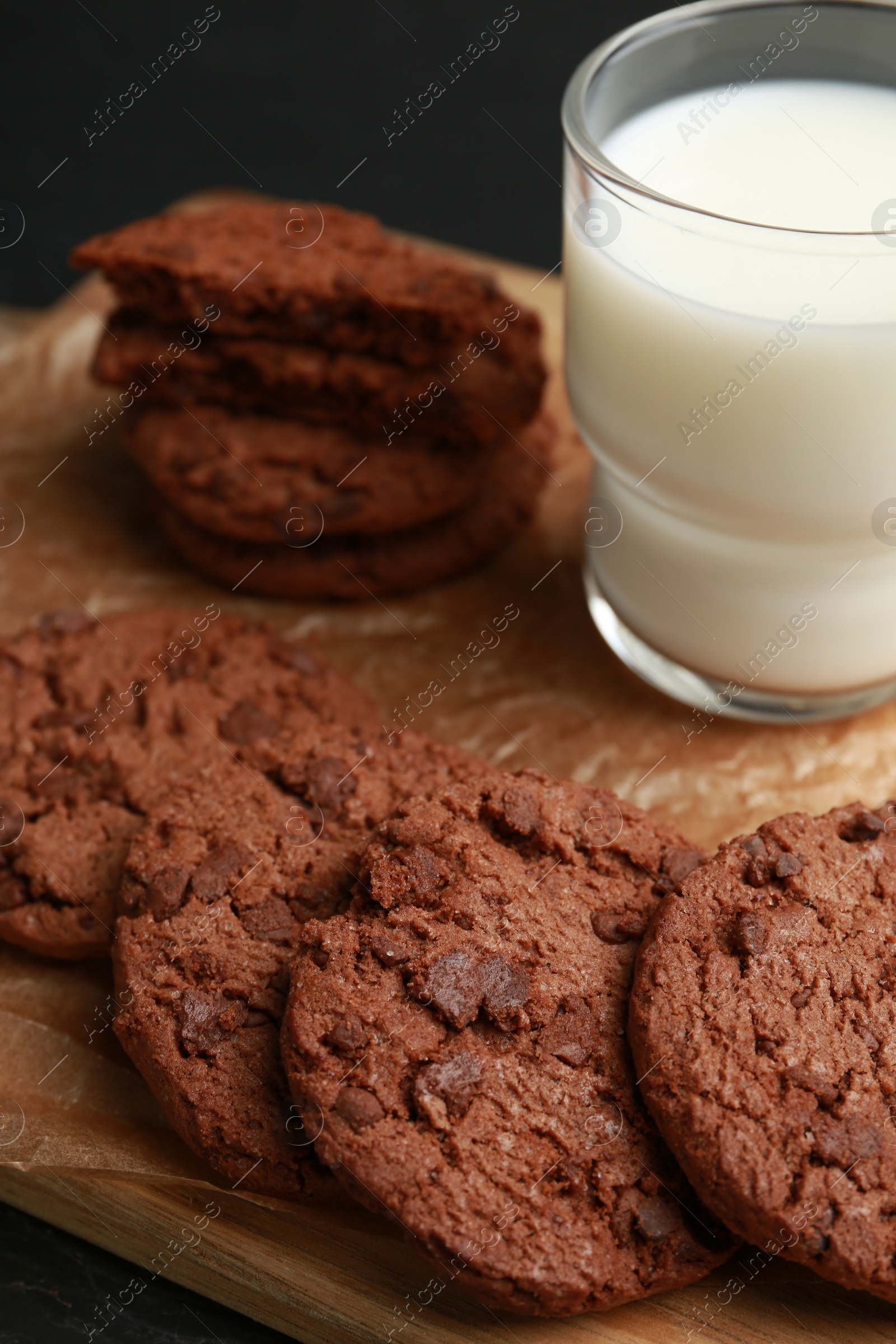 Photo of Board with tasty chocolate cookies and glass of milk on table, closeup