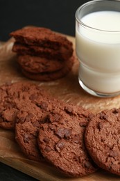 Photo of Board with tasty chocolate cookies and glass of milk on table, closeup