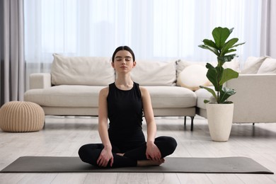 Beautiful girl meditating on yoga mat at home