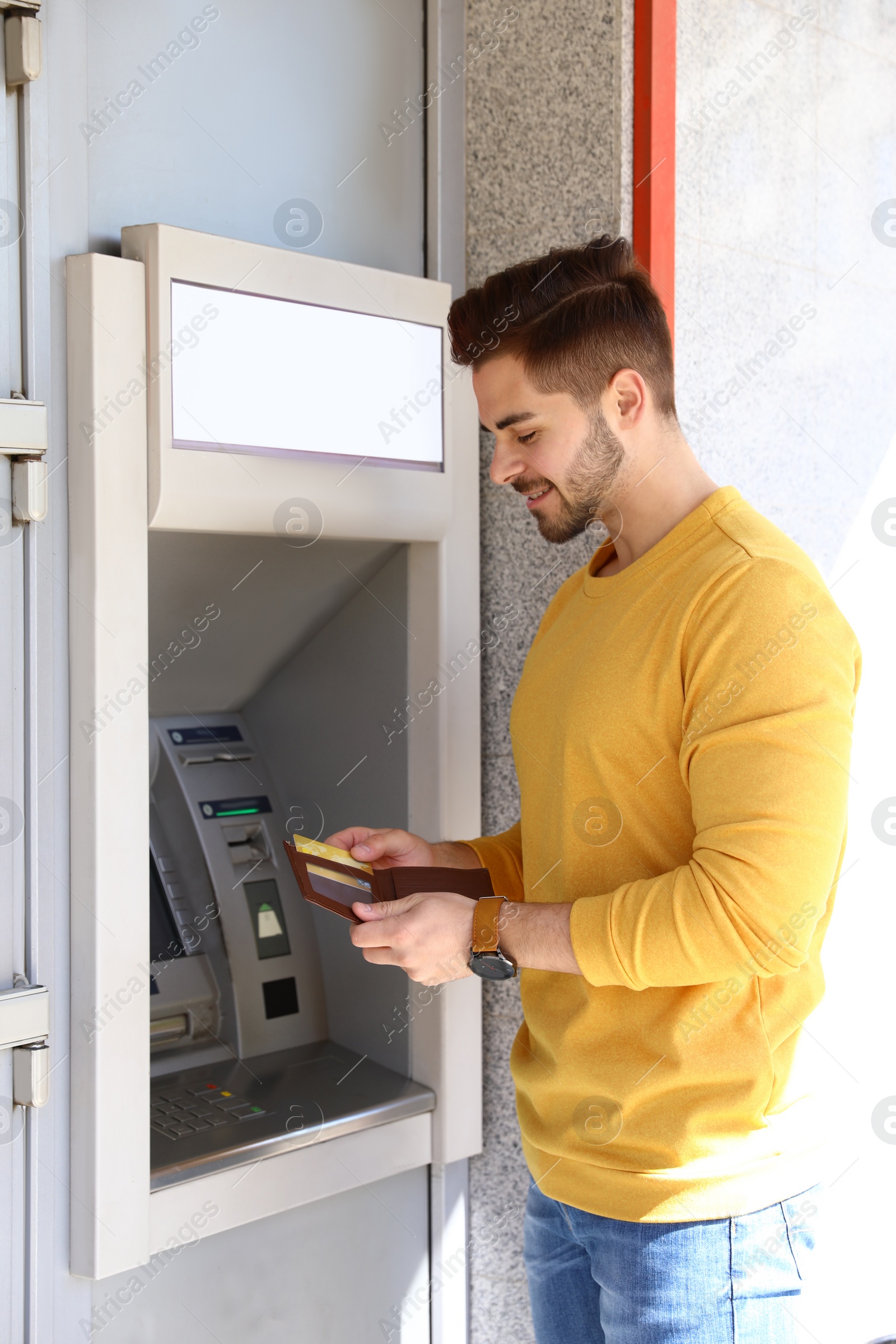 Photo of Young man with credit card near modern cash machine outdoors