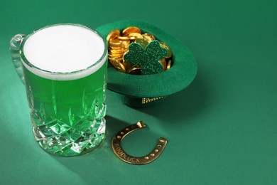 Photo of St. Patrick's day party. Green beer, leprechaun hat with gold, horseshoe and decorative clover leaf on green background. Space for text