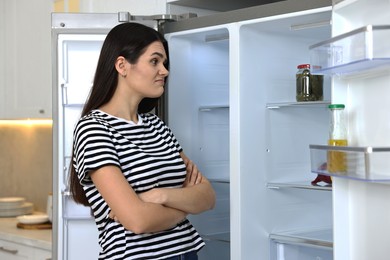 Upset woman near empty refrigerator in kitchen