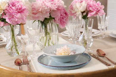 Stylish table setting with beautiful peonies and golden cutlery indoors