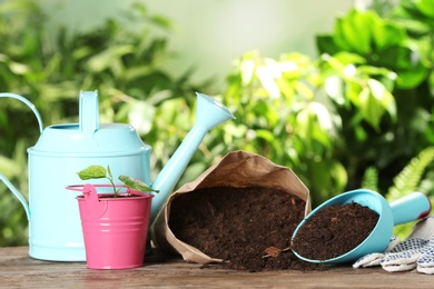 Composition with bag of soil and gardening equipment on wooden table against blurred background, space for text