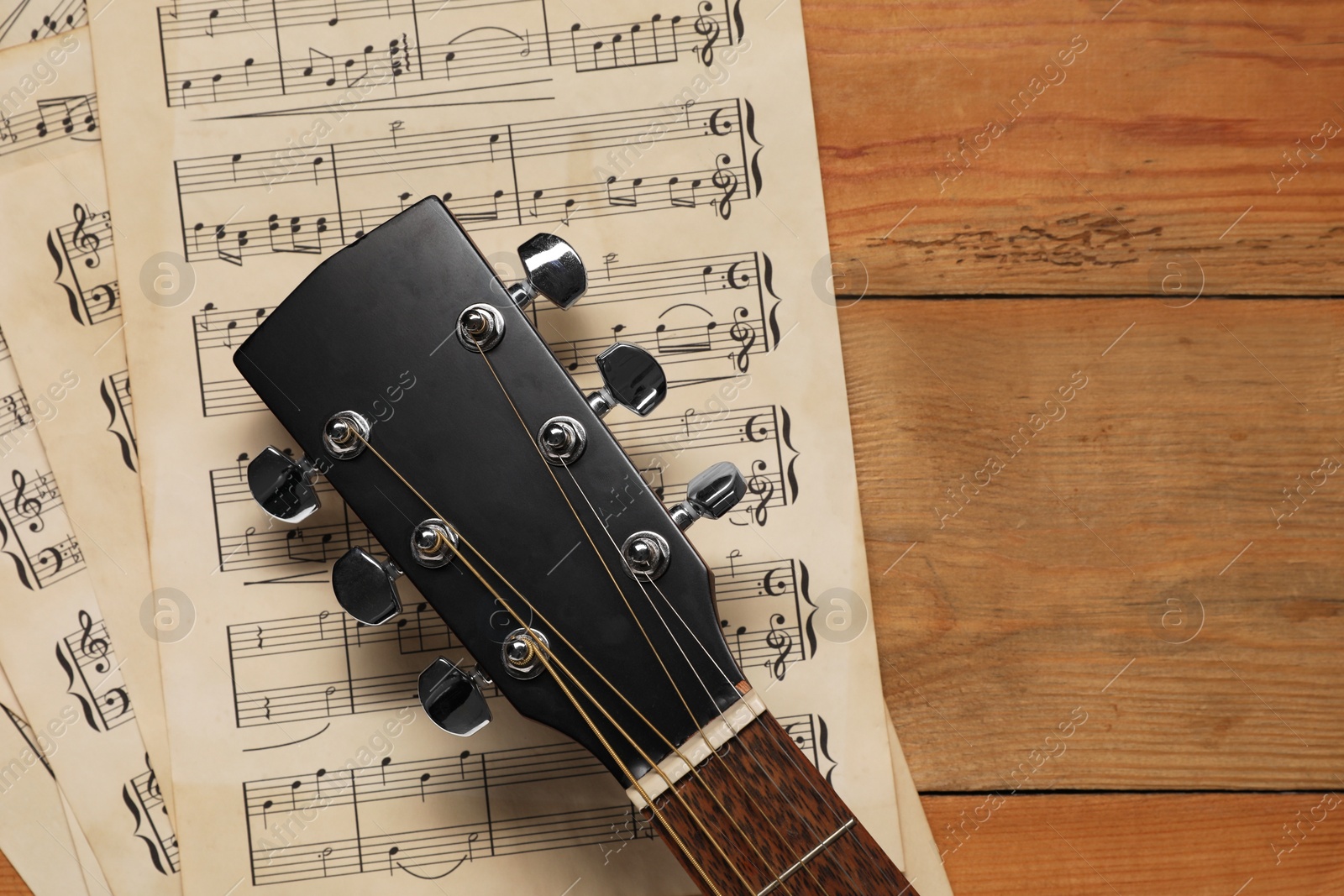 Photo of Paper sheets with music notes and acoustic guitar on wooden table, top view