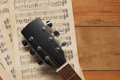 Photo of Paper sheets with music notes and acoustic guitar on wooden table, top view