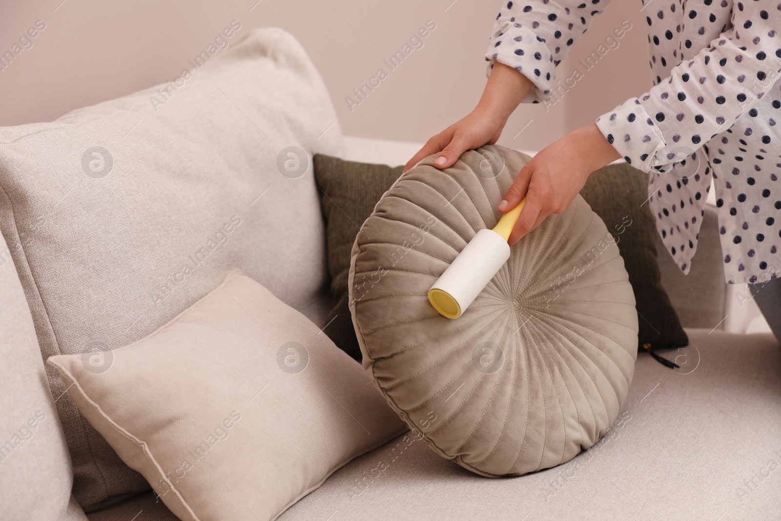 Photo of Young woman cleaning pillow with lint roller on sofa, closeup