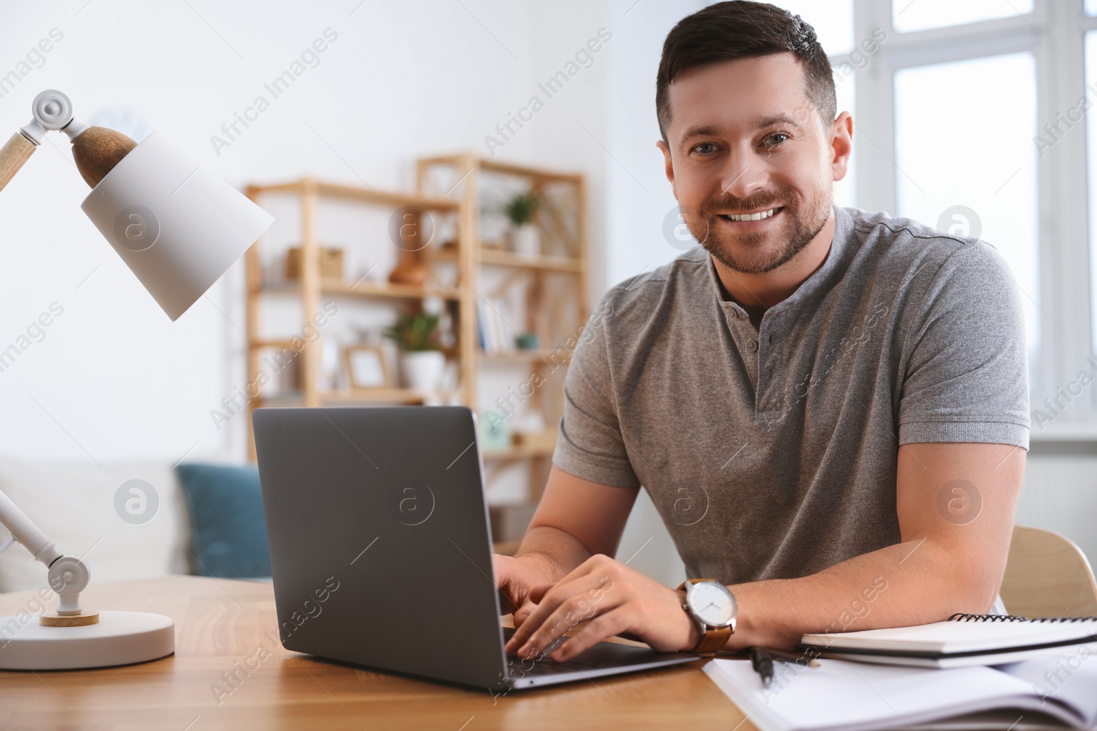 Photo of Happy man working on laptop at wooden desk in room