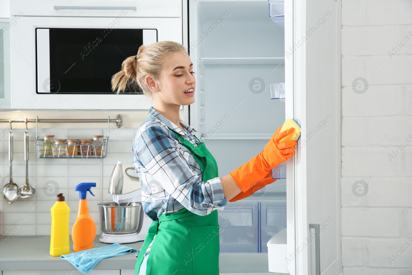 Photo of Woman in rubber gloves cleaning empty refrigerator at home
