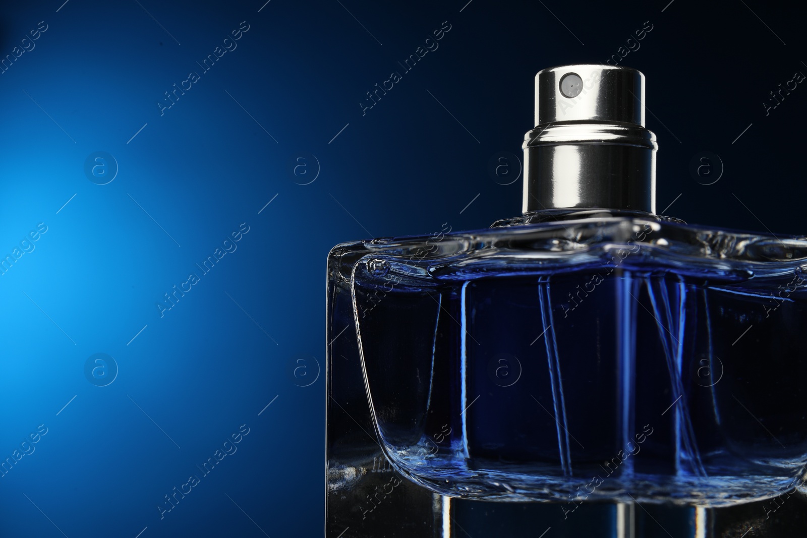 Photo of Luxury men`s perfume in bottle against dark blue background, closeup. Space for text