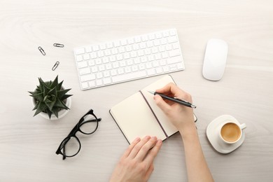 Photo of Woman writing in notebook at light wooden table, top view